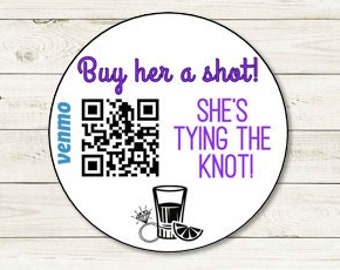 May include: White circular sticker with purple text that reads "Buy her a shot! She's tying the knot!" A black and white QR code is next to the text. The words "venmo" are written vertically on the left side of the QR code. A black and white illustration of a shot glass with a lime wedge is below the text.