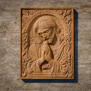 May include: A wooden carving of Jesus Christ with his hands clasped in prayer. The carving is framed with a detailed floral design and is mounted on a stone wall.