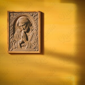 May include: A wooden carving of a person with their hands clasped in prayer, framed in a light brown wood frame. The carving is on a yellow wall.