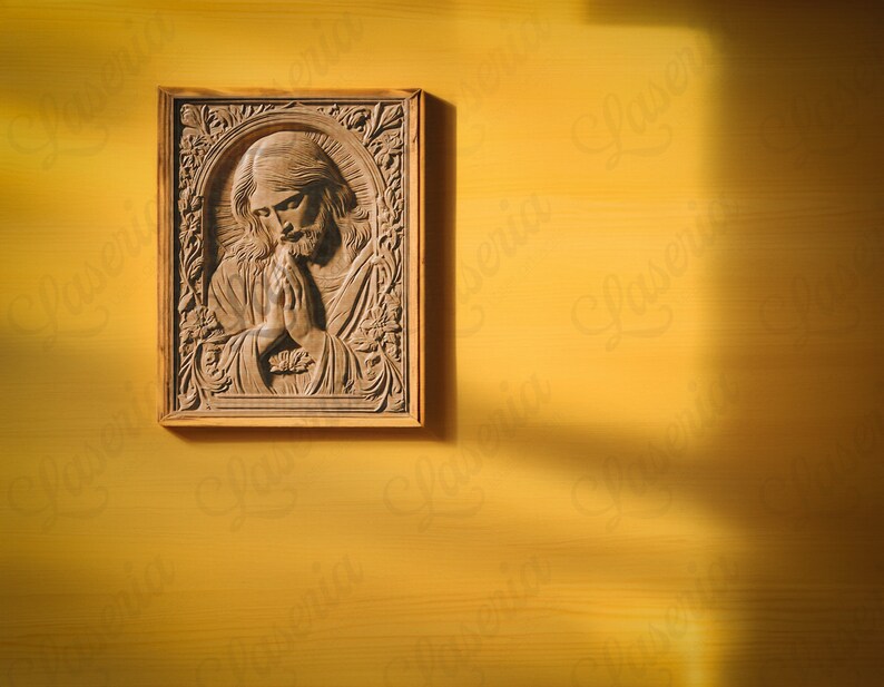 May include: A wooden carving of a person with their hands clasped in prayer, framed in a light brown wood frame. The carving is on a yellow wall.