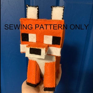 May include: Sewing pattern for a Minecraft fox plush toy. The pattern includes instructions for creating a red, white and black fox with a blocky design.