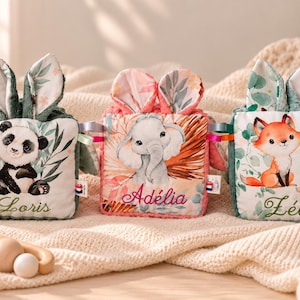 Peut inclure: Trois cubes sensoriels en peluche carrés avec des oreilles de lapin, chacun illustré d'un animal différent : un panda nommé Loris, un éléphant nommé Adélia et deux renards nommés Zélie. Chaque cube possède des étiquettes en tissu colorées.