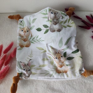 May include: A white baby security blanket with a pattern of watercolor bunnies and green leaves. The blanket has brown plush corners. The overall design is soft and inviting, perfect for a nursery or baby gift.