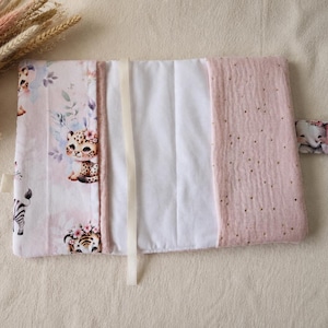 Pu&ograve; includere: Un fasciatoio rettangolare in tessuto con sfondo rosa chiaro e illustrazioni di cuccioli di animali tra cui un leopardo, una tigre e una zebra. Include un pannello centrale bianco, un pannello laterale rosa testurizzato con puntini dorati e una chiusura a pressione.