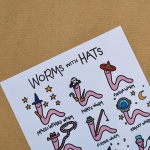 May include: A white card with the text "WORMS WITH HATS" at the top. The card features illustrations of pink worms wearing different hats, including a pirate hat, a wizard hat, a fiesta hat, a space helmet, a cowboy hat, and a fishing hat. Each worm has a unique name written below it.