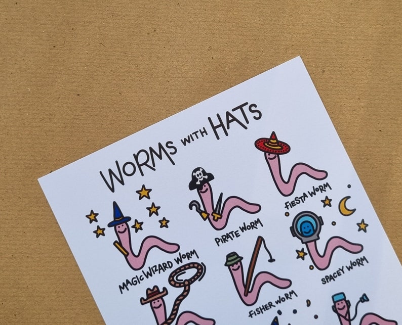 May include: A white card with the text "WORMS WITH HATS" at the top. The card features illustrations of pink worms wearing different hats, including a pirate hat, a wizard hat, a fiesta hat, a space helmet, a cowboy hat, and a fishing hat. Each worm has a unique name written below it.