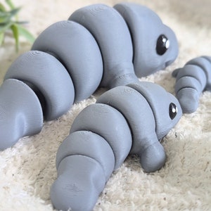 May include: Three gray segmented toy animals with black eyes. The largest animal is lying down, the middle animal is standing, and the smallest animal is lying down.