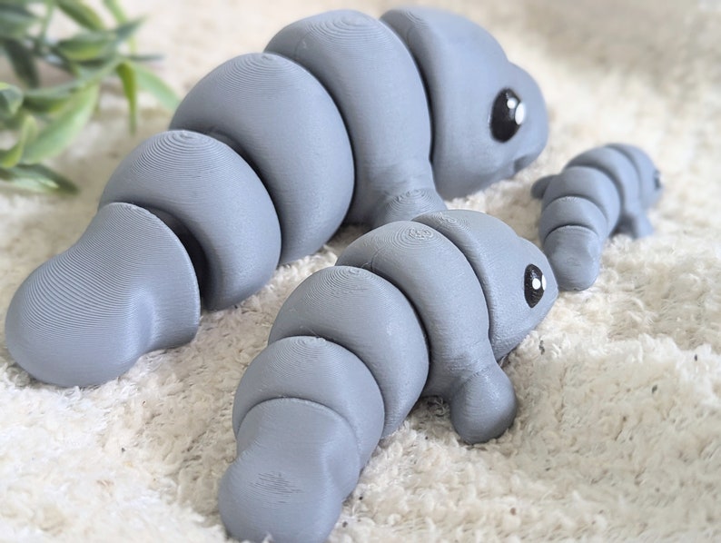 May include: Three gray segmented toy animals with black eyes. The largest animal is lying down, the middle animal is standing, and the smallest animal is lying down.