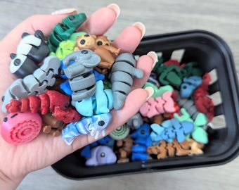 May include: A hand holding a variety of colorful small plastic animal figurines. The figurines are in a basket with more figurines.