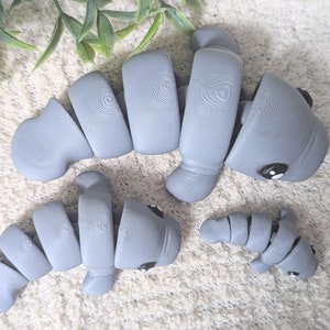 May include: Three gray ceramic manatee figurines. The largest manatee is curled in a C shape. The medium-sized manatee is curled in a U shape. The smallest manatee is curled in a J shape.