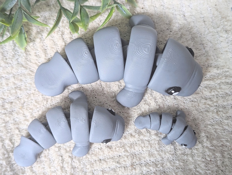 May include: Three gray ceramic manatee figurines. The largest manatee is curled in a C shape. The medium-sized manatee is curled in a U shape. The smallest manatee is curled in a J shape.