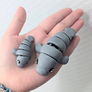 May include: Two gray, segmented, articulated, manatee figurines. The larger manatee is about 5 inches long and the smaller manatee is about 3 inches long.