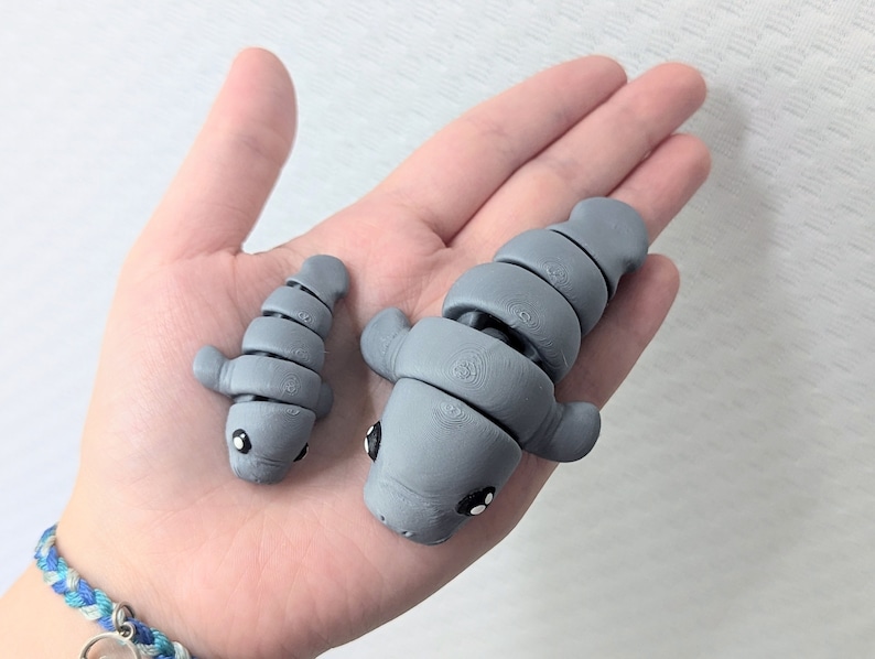 May include: Two gray, segmented, articulated, manatee figurines. The larger manatee is about 5 inches long and the smaller manatee is about 3 inches long.