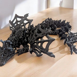May include: A black, 3D printed dragon sculpture with intricate, web-like details. The dragon is posed in a dynamic, curled position with its wings spread out.