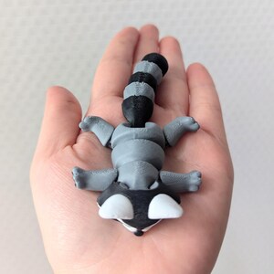Peut inclure: Une petite figurine de raton laveur gris et noir avec une queue enroul&eacute;e. La figurine est en plastique et pr&eacute;sente un design d&eacute;taill&eacute;.