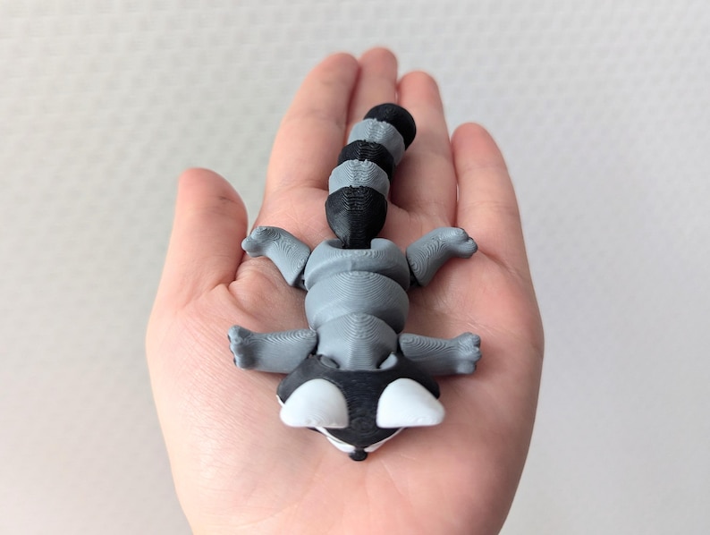 Peut inclure: Une petite figurine de raton laveur gris et noir avec une queue enroul&eacute;e. La figurine est en plastique et pr&eacute;sente un design d&eacute;taill&eacute;.
