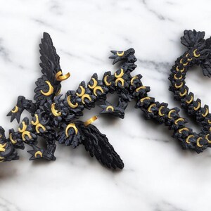 May include: A black and gold dragon figurine with crescent moon details. The dragon is posed in a curled position with its wings spread out.