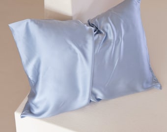 Könnte beinhalten: Zwei hellblaue Satin-Kissenbezüge, gefaltet und auf einer weißen Oberfläche platziert.