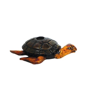 May include: A handcrafted turtle-shaped decorative item. The turtle has a dark brown shell with a circular opening and orange-yellow head and limbs. The item is made of a carved material.