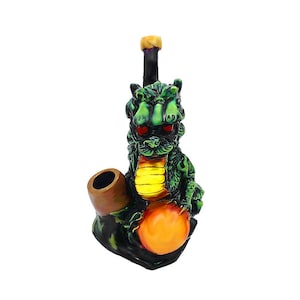 May include: A green dragon-shaped pipe with red eyes and a yellow belly. The pipe has a brown bowl and a black stem with a yellow mouthpiece. The dragon is holding an orange orb.