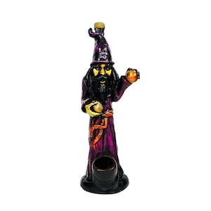 May include: A wizard figurine with a long purple robe and a matching pointed hat. The wizard has a long black beard and holds a golden orb in each hand. The figurine has a dark brown bowl at the base and is a decorative item.