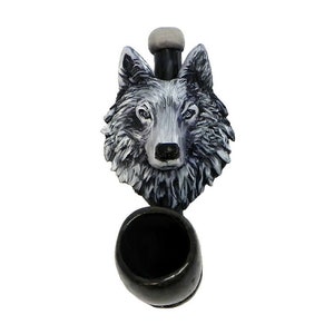 May include: A decorative pipe featuring a wolf's head in shades of gray and white. The pipe has a black bowl and a gray mouthpiece. The wolf's fur is detailed, and the pipe is designed to be held.