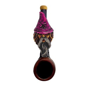May include: A novelty pipe featuring a gnome design. The pipe has a dark brown bowl and stem, with a carved gnome head in shades of brown, gray, and pink. The gnome wears a pink hat and has a long, gray beard.