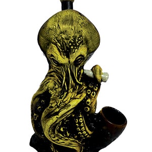 May include: A ceramic pipe shaped like an octopus with a yellow and black paint design. The pipe has a bowl on the side and a mouthpiece on the top.
