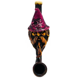 May include: A carved wooden tobacco pipe featuring a wizard's face with a long beard and a pointed hat. The hat is a deep magenta color, and the beard is a mix of gold and brown. The pipe's bowl is dark brown.