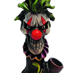 May include: A ceramic pipe shaped like a clown with a green mohawk, red nose, and purple collar. The pipe has a black and green design with an orange accent.