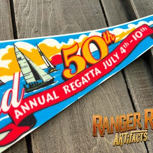 May include: A pennant with a nautical theme, featuring sailboats on a blue sea under a yellow and orange sky. The pennant celebrates the 50th Annual Regatta, July 4th-10th, with red ribbon text. The Ranger Rob Artifacts logo is in the bottom right.