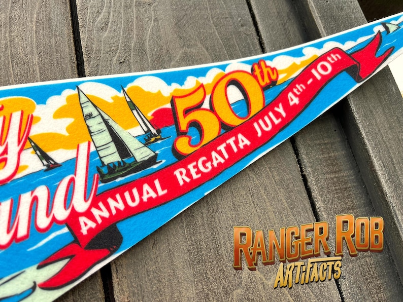 May include: A pennant with a nautical theme, featuring sailboats on a blue sea under a yellow and orange sky. The pennant celebrates the 50th Annual Regatta, July 4th-10th, with red ribbon text. The Ranger Rob Artifacts logo is in the bottom right.