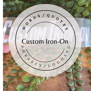 May include: A white circle with the text "Words/Quotes Phrases/Logos" around the edge and "Custom Iron-On" in the centre.