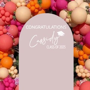 May include: A pink, orange, and peach balloon arch with a white sign that says "Congratulations Cassidy Class of 2023".