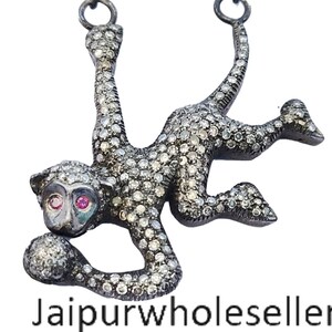 以下が含まれることがあります： ダイヤモンドで飾られたシルバーのサルペンダントネックレス。サルは手にボールを持っており、ピンクの目があります。ネックレスはシルバーチェーンです。