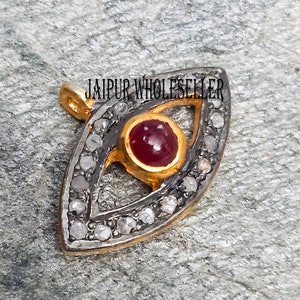 May include: A gold and silver evil eye pendant with a red gemstone in the center. The pendant is surrounded by small diamonds.
