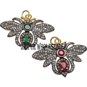May include: Two silver and gold butterfly charms with pave diamond accents. One charm features a green gemstone and the other features a red gemstone.