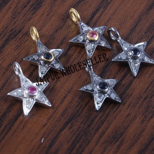 May include: Five star-shaped pendants with small gemstones. The pendants are silver-coloured with small, clear stones around the edges. Each star has a different coloured gemstone in the centre, including red, blue, and yellow. The text "JAIPUR WHOLESALER" is visible.