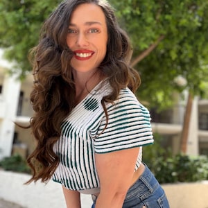 May include: A short-sleeved, cropped crochet top featuring a pattern of vertical dark green and white stripes, paired with blue denim jeans. The top has a V-neckline and a textured, hand-stitched appearance with a visible knit construction.