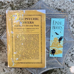 May include: A rectangular book titled Your Psychic Powers And How to Develop Them by Hereward Carrington, Ph.D., with a tan cover, alongside a light blue bookmark featuring the text Eisiau Books, a silhouette of a cat, an owl, and a bat.