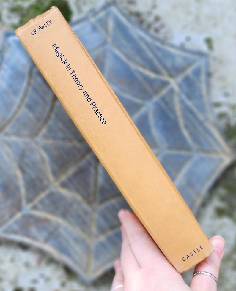 May include: A tan book spine with the title "Magick in Theory and Practice" by Crowley. The publisher is "Castle". The spine is set against a blurred, patterned background.