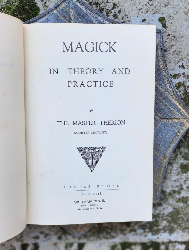 May include: An open book with the title "MAGICK IN THEORY AND PRACTICE" by The Master Therion (Aleister Crowley). The book has an off-white cover with black text and a decorative emblem. Published by Castle Books, New York.
