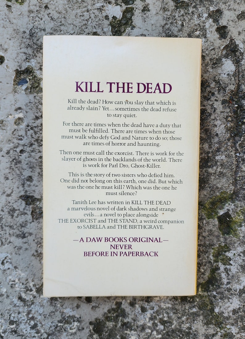 May include: A paperback book cover with the title "KILL THE DEAD" in large purple text. The back cover features descriptive text about the novel, including the author, Tanith Lee, and a summary of the plot.