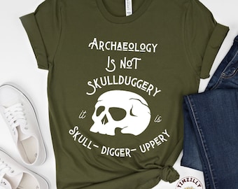 May include: A green t-shirt with a white skull graphic and the text "Archaeology is not skullduggery, it is skull-digger-upperry".