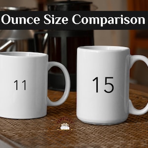 May include: Two white ceramic mugs with black numbers on them. The mug on the left says "11" and the mug on the right says "15". The mugs are on a brown wicker surface.