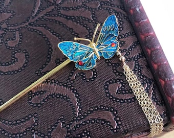 May include: A gold hair stick with a blue butterfly design. The butterfly has red accents and a gold chain tassel.