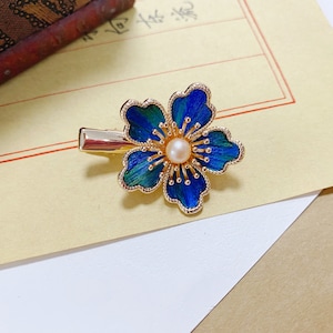 May include: A gold hair clip with a blue and green enamel flower design and a pearl in the centre.