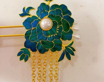 May include: A gold hair clip with a blue and green flower design and a pearl accent. The clip has a chain with gold tassels.