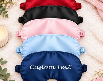 May include: A stack of five satin sleep masks in red, black, light pink, light blue, and navy blue. Each mask features an elasticated strap. The bottom navy blue mask displays the white embroidered text Custom Text in a script font.