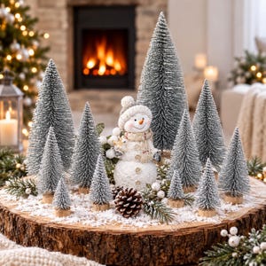 May include: A decorative snowman figurine wearing a knit hat and scarf, surrounded by multiple flocked bottle brush pine trees of varying heights, pinecones, and white berries on a circular wooden log slice base covered in artificial snow.